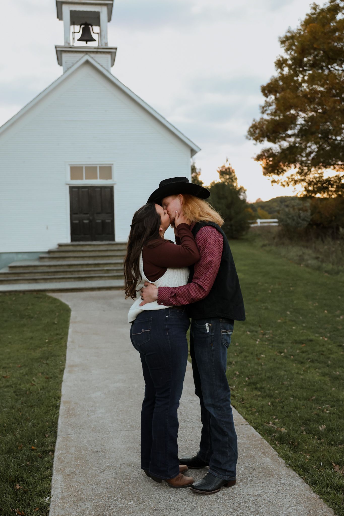 Couple sharing a kiss outside a white chapel at sunset in autumn.