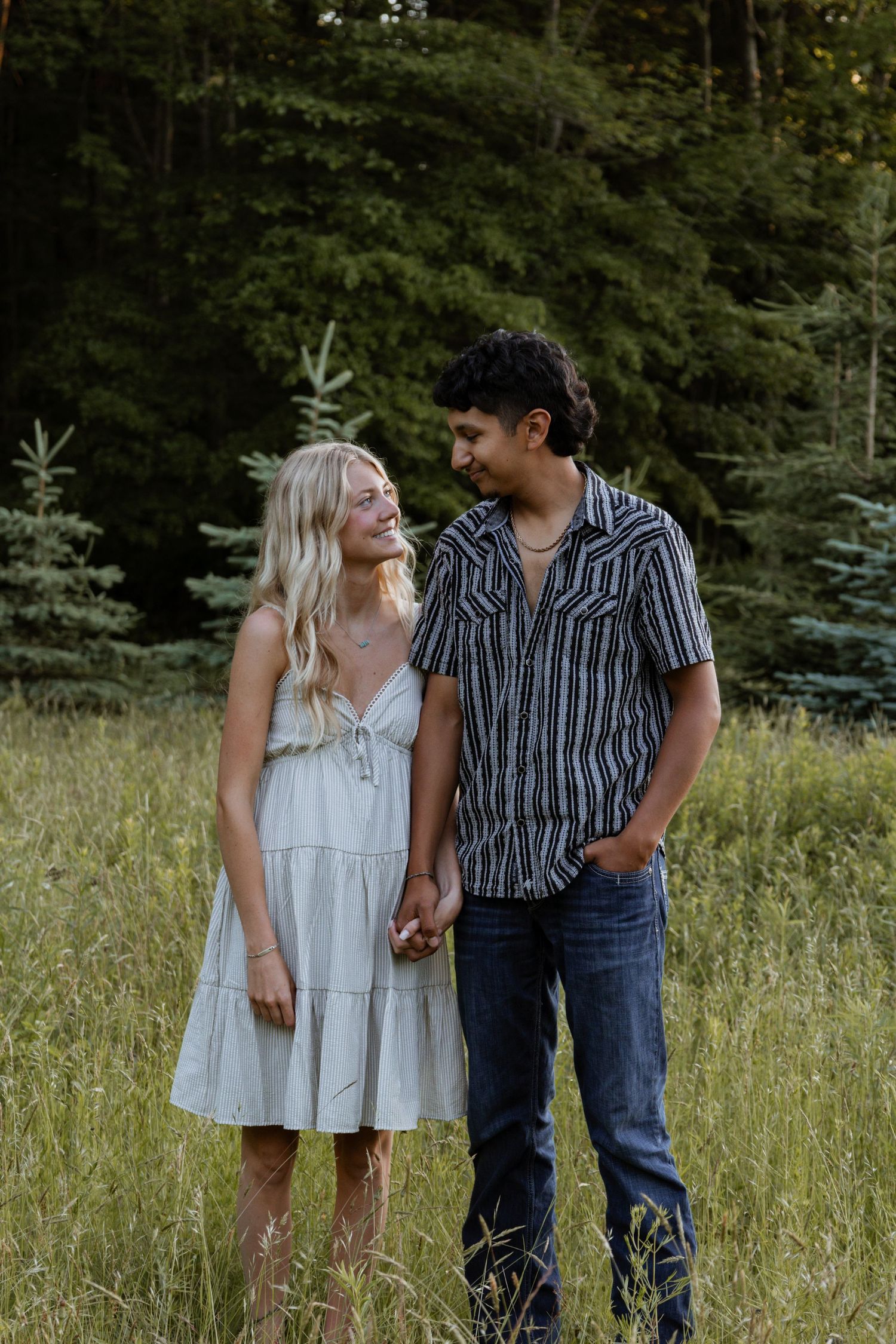 Happy couple holding hands and smiling at each other in a lush green meadow.
