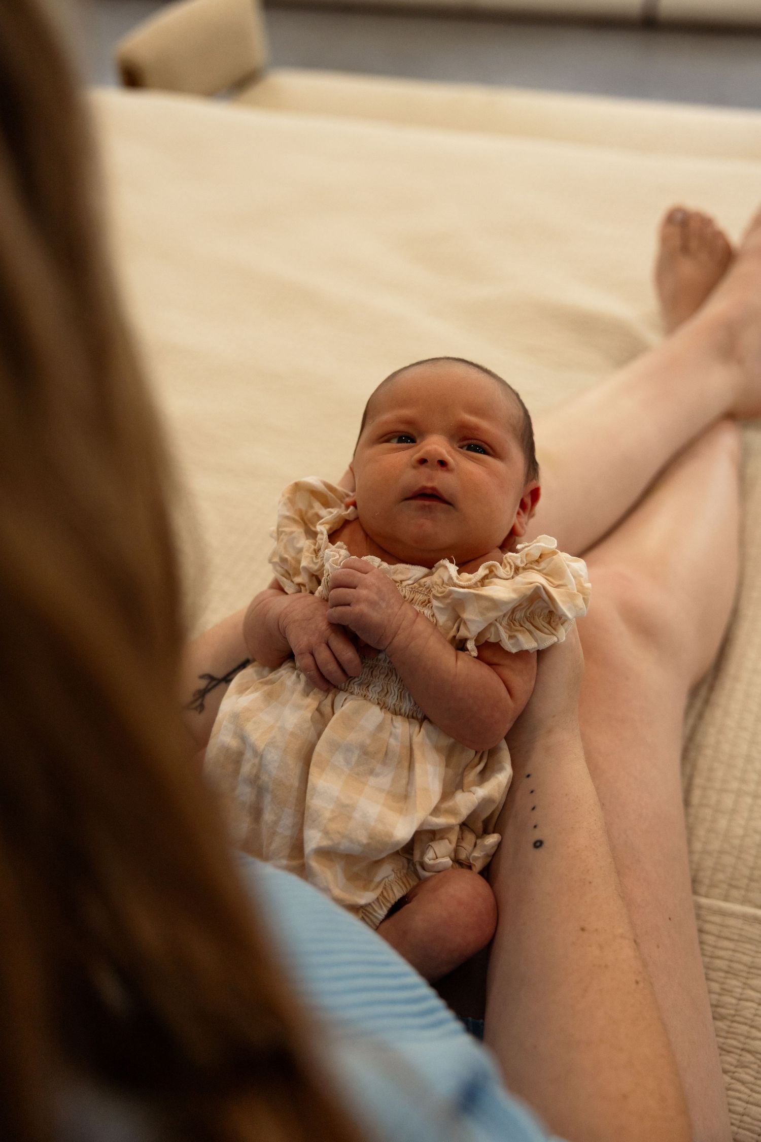 Newborn baby in a floral romper lying on a bed, looking up at mother during a tender postpartum moment.