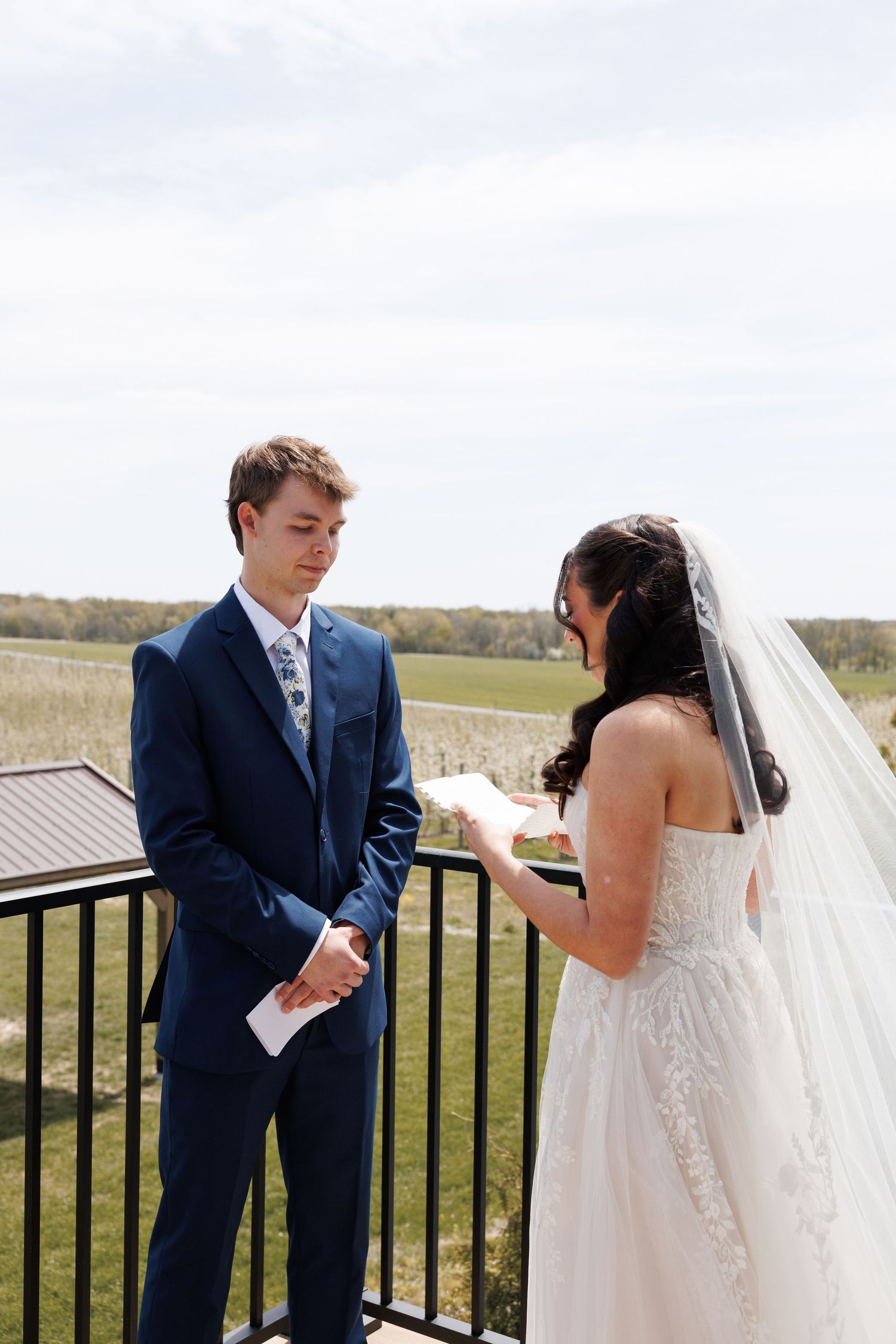 Bride reads heartfelt personal vows to her groom on a balcony overlooking a scenic countryside.