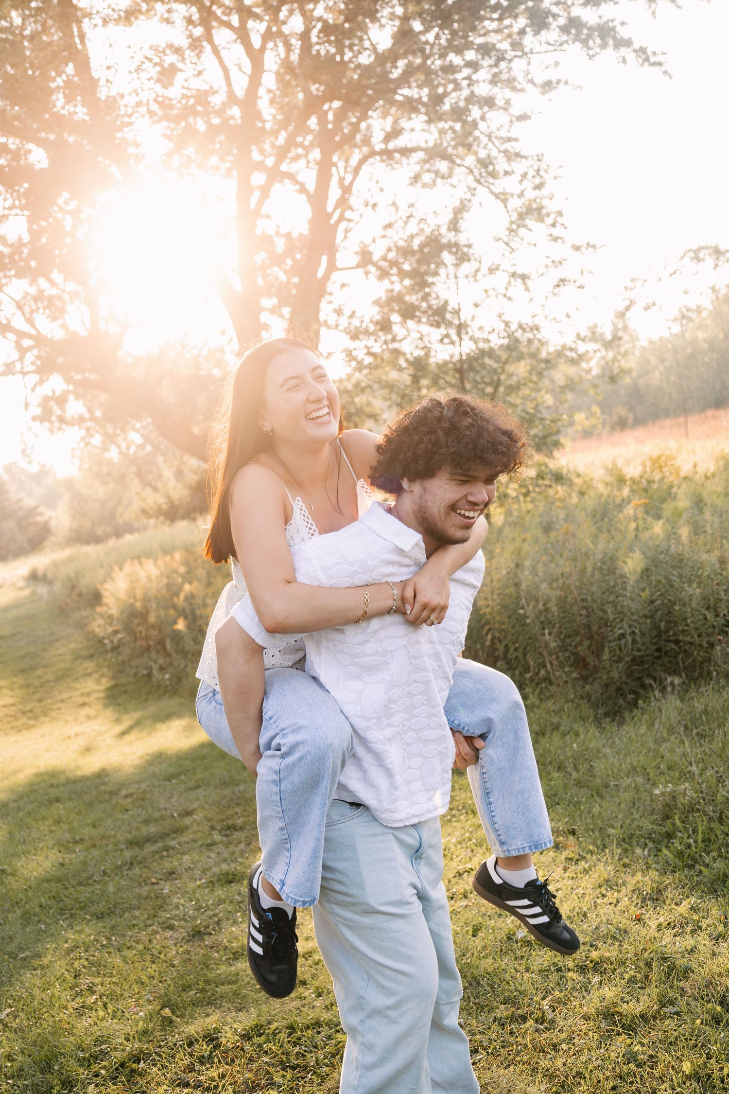 A joyful couple enjoying a piggyback ride outdoors at golden hour, laughing together in a sunny green park.