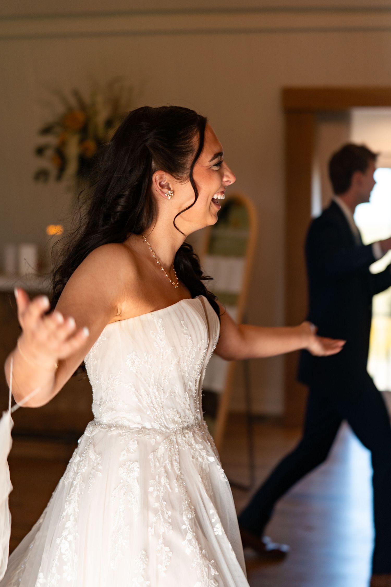 Joyful bride in strapless lace wedding gown laughing and dancing at her wedding reception.