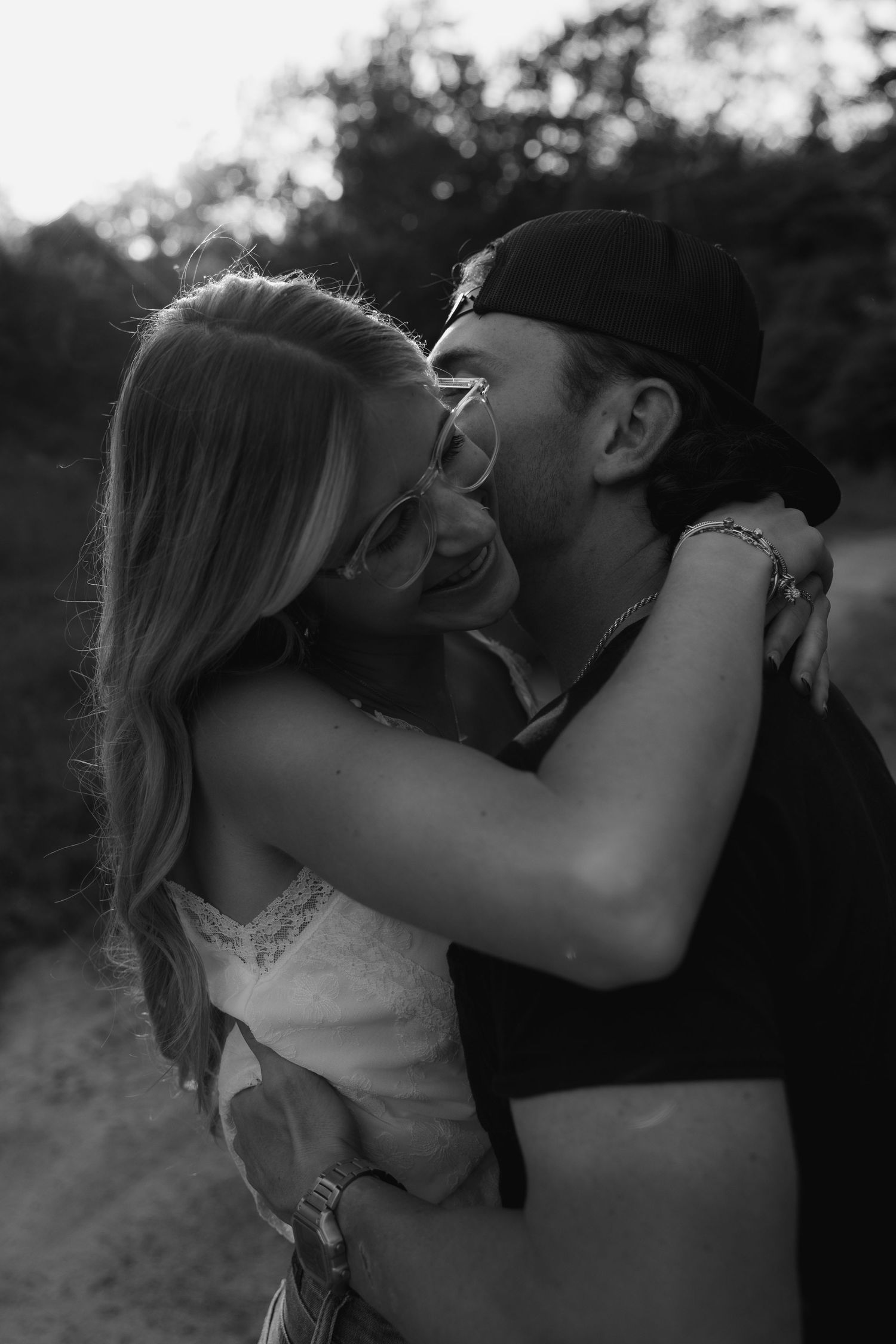 Black and white photo of a smiling couple embracing and laughing together outdoors in a candid romantic moment.