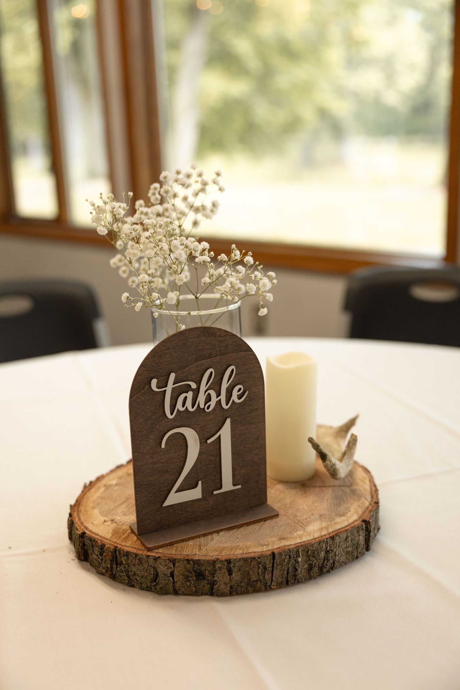 Rustic wedding table centerpiece with wooden Table 21 sign, candle, and baby's breath on log slice.
