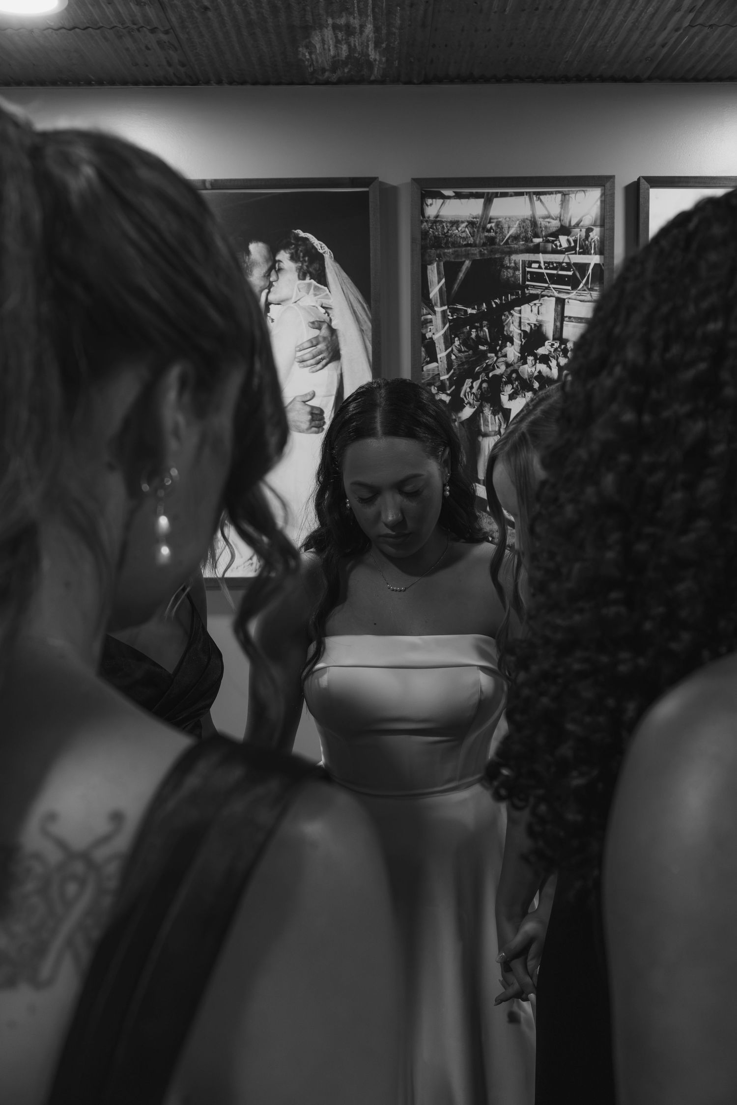 Bride in white gown surrounded by bridesmaids in black and white wedding preparation photo.