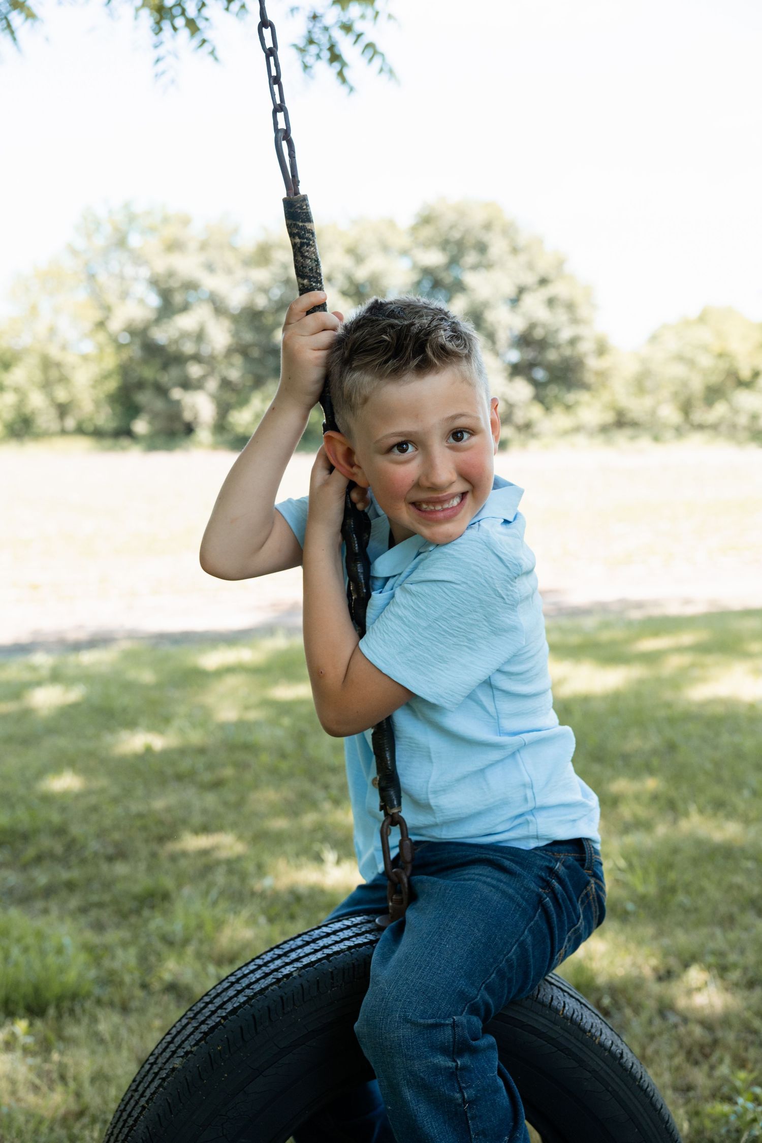 Smiling young boy riding a tire swing outdoors on a sunny day in a green park.