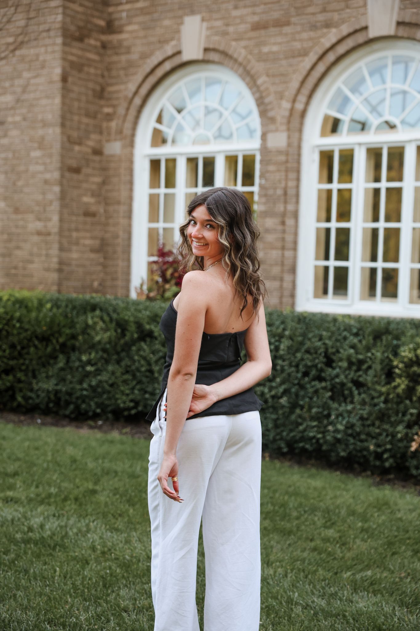 Young woman in black tube top and white pants outside brick building.