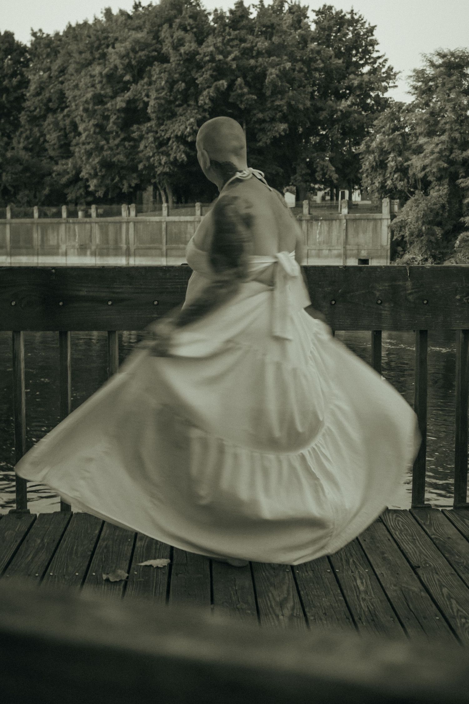 A sepia-toned motion blur photo of a person in a white dress twirling on a wooden waterfront dock.