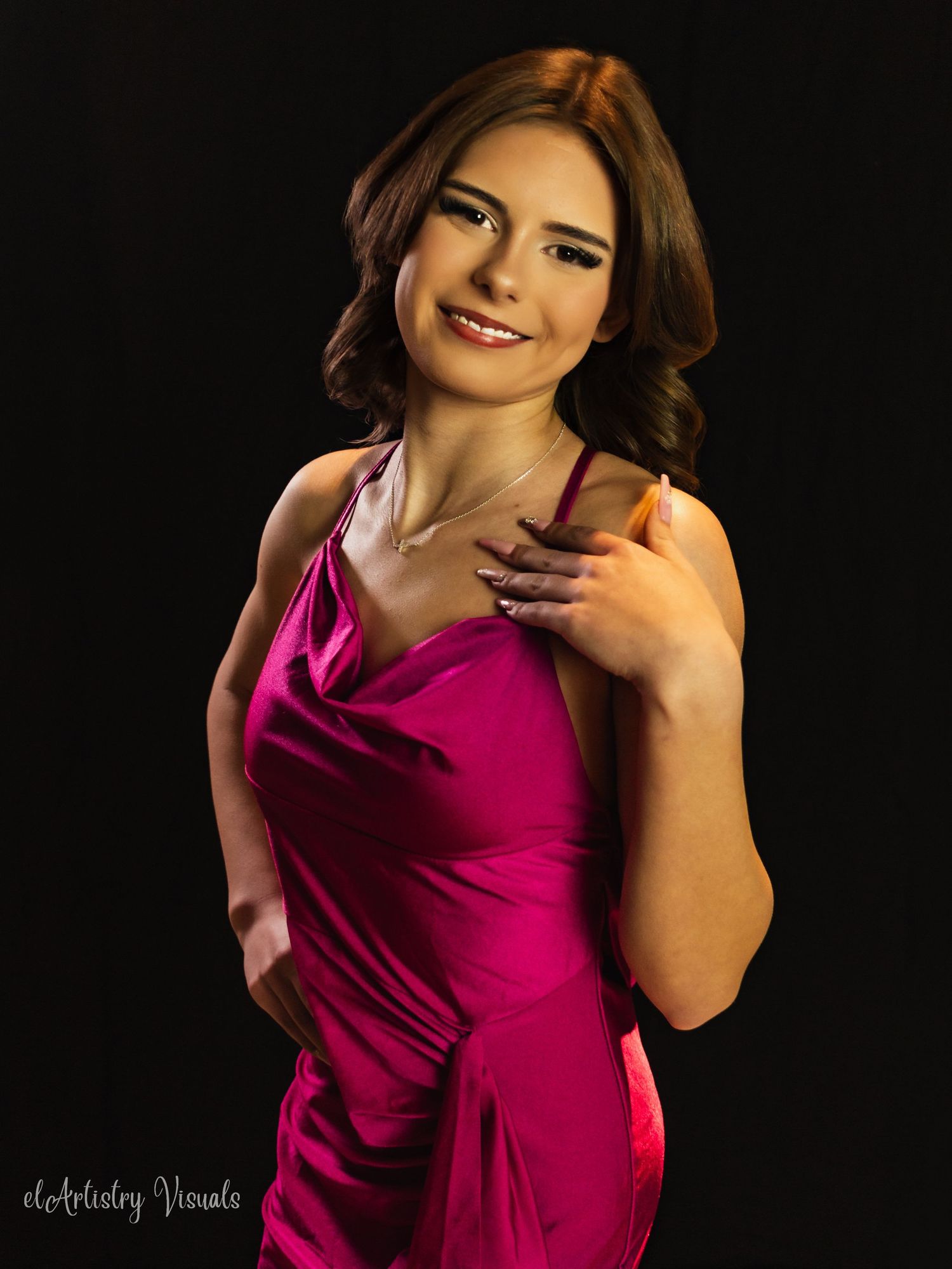Young woman in a magenta satin halter dress posing against a dark background in a professional portrait.