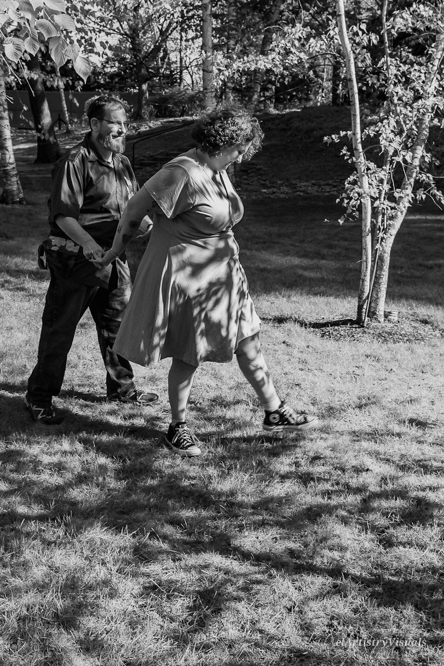 Black and white photo of a couple holding hands and walking together in a sunlit park.
