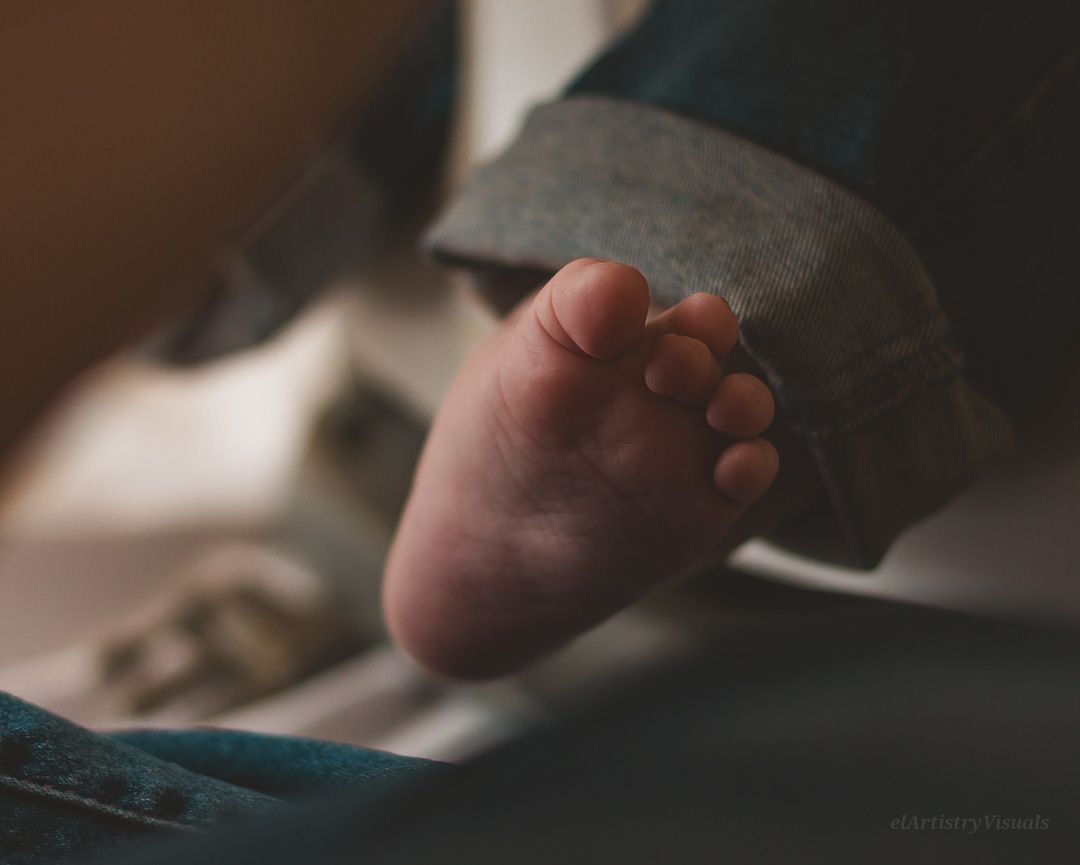 Close-up of a newborn baby's tiny foot resting against a soft teal fabric in warm light.