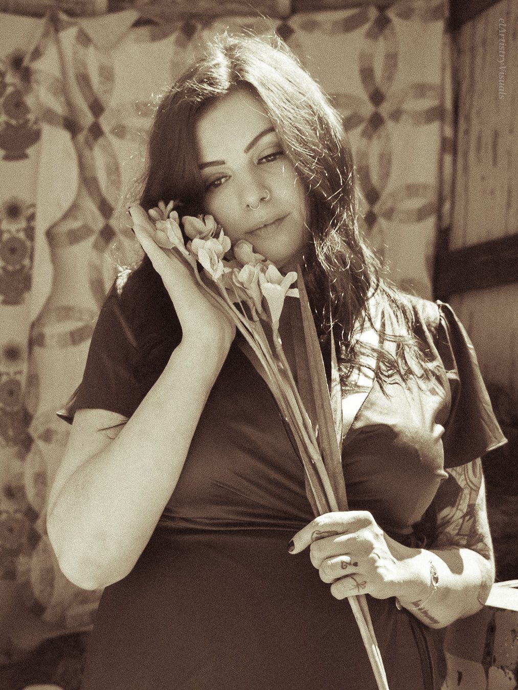 Sepia-toned portrait of a woman resting her cheek on white daffodils while holding a bouquet indoors.