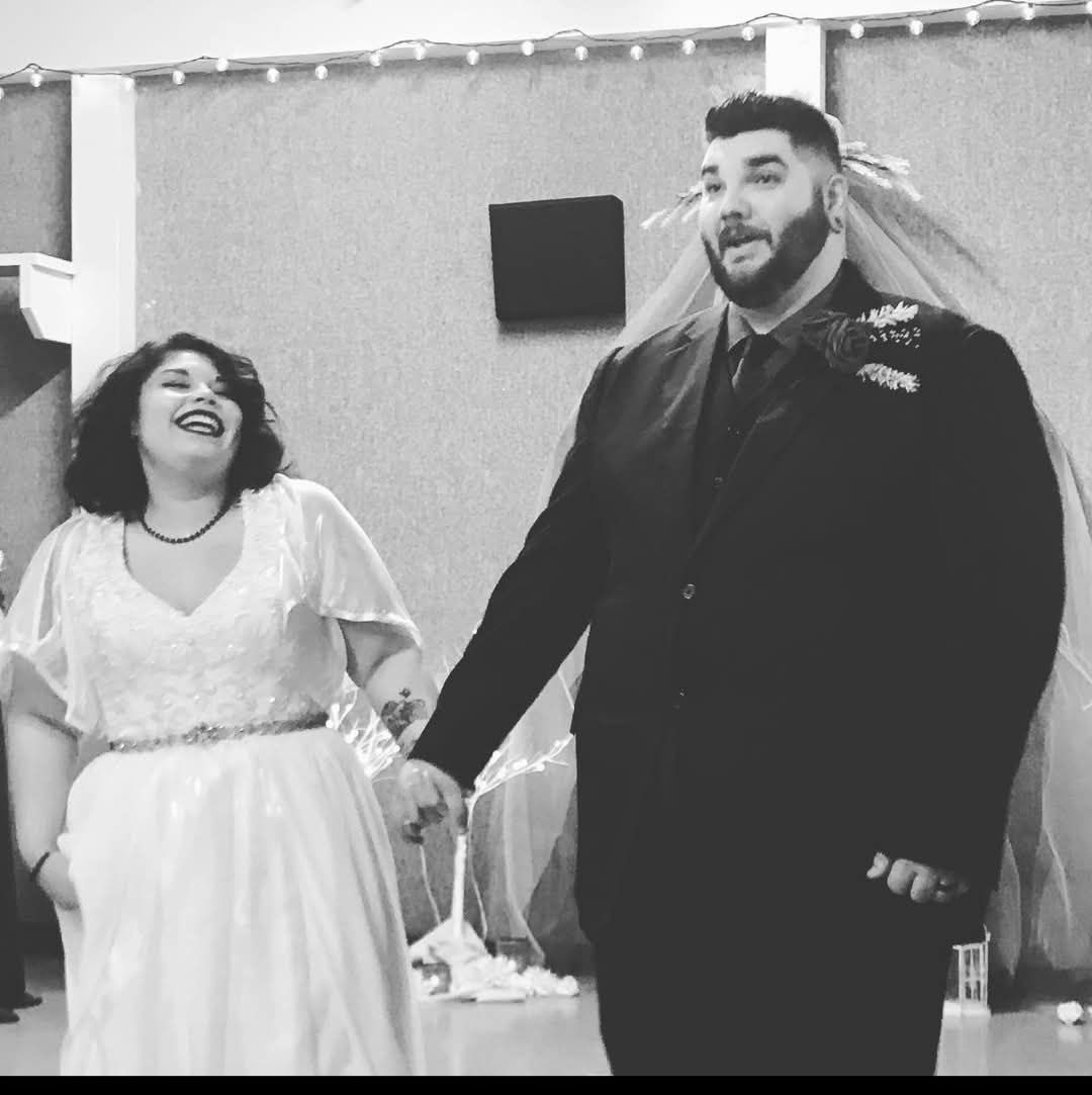 A joyful bride and groom hold hands and laugh together in a black and white wedding reception photo.