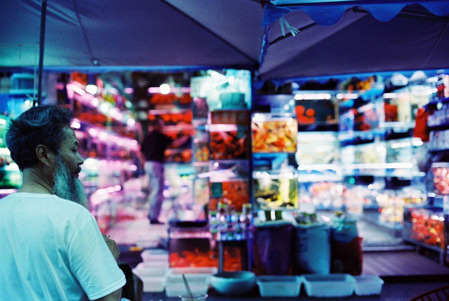 Man browsing colorful illuminated market stall displays at a vibrant Chinese night market.