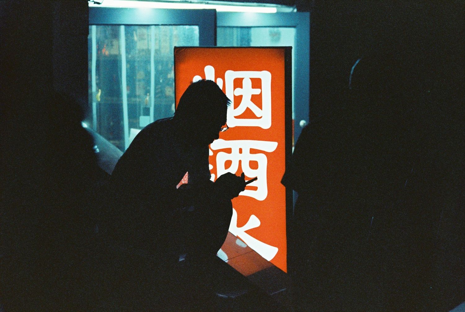 Silhouette of a person against a glowing orange Chinese sign at night.