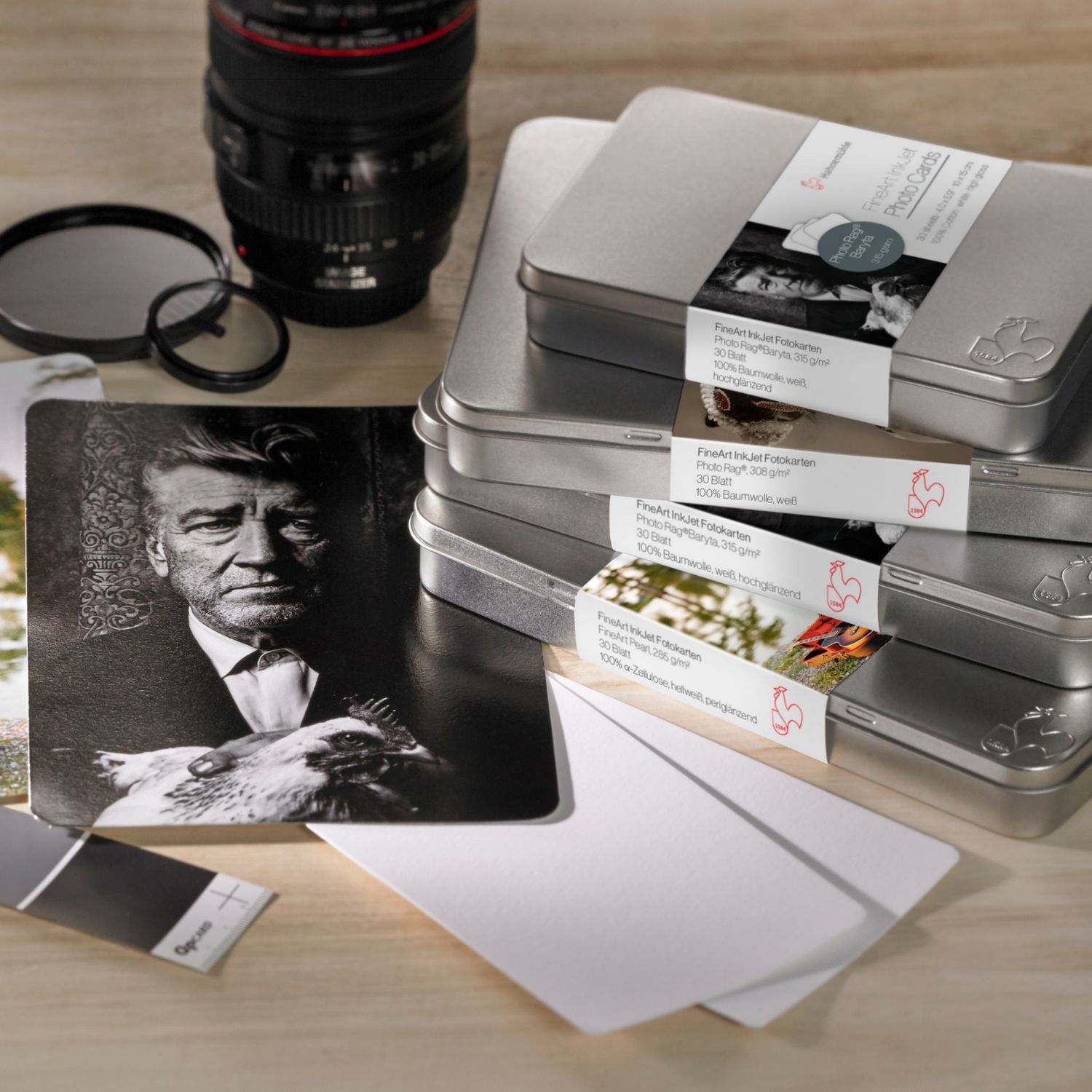 Hahnemuhle fine art paper sample sets in metal tins with black and white portrait prints and camera lens.