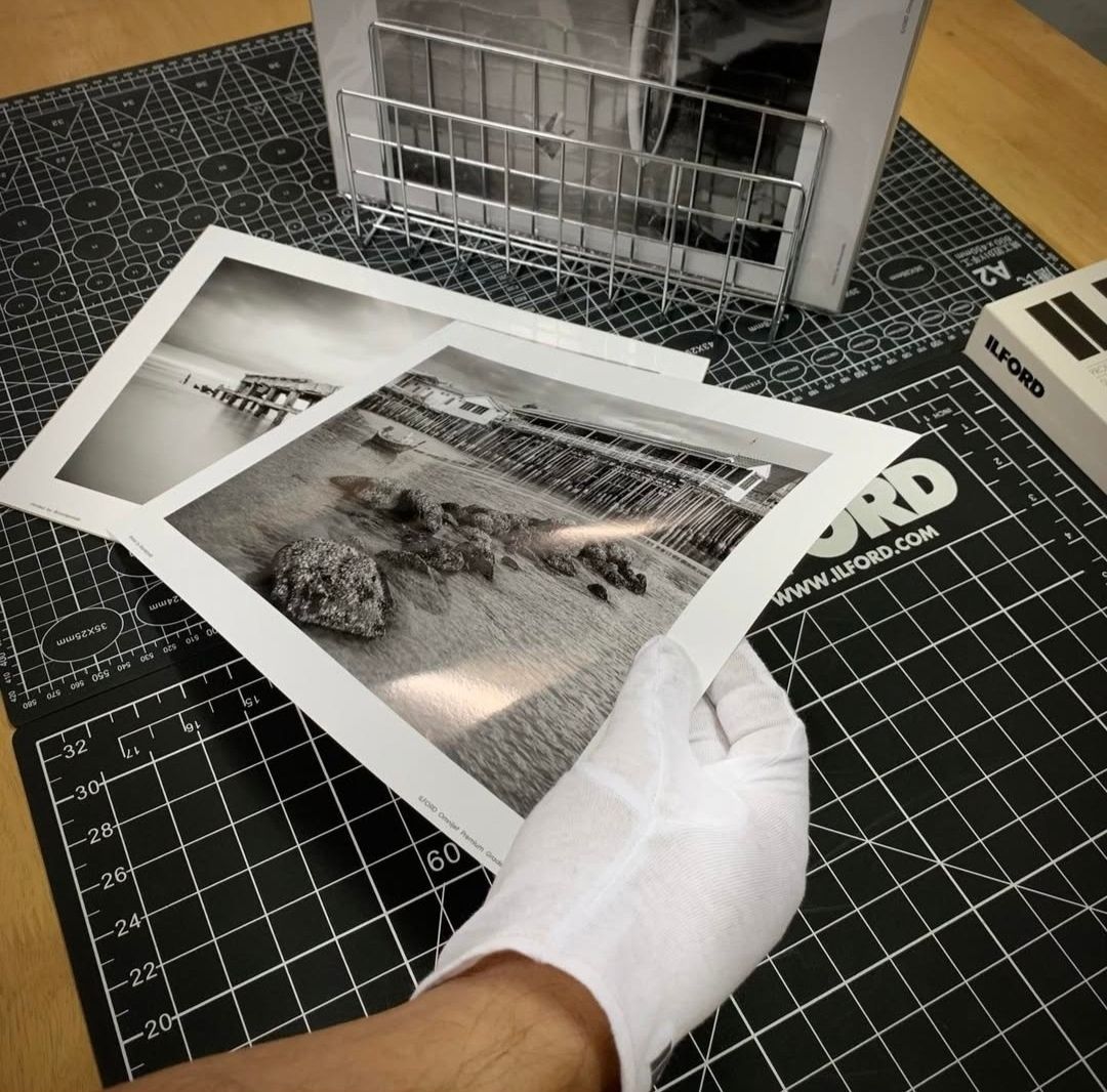 Gloved hands holding a black and white fine art print over a cutting mat in a photography studio.