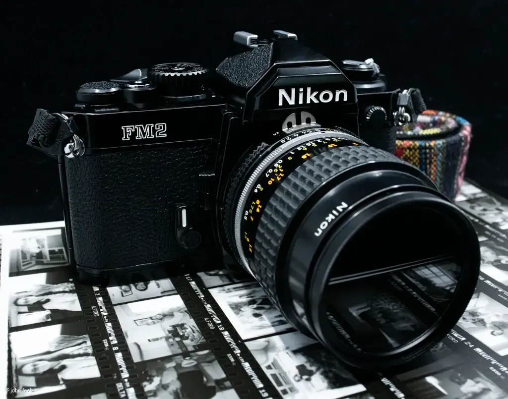 Nikon FM2 35mm film SLR camera with lens on black and white film strips background.