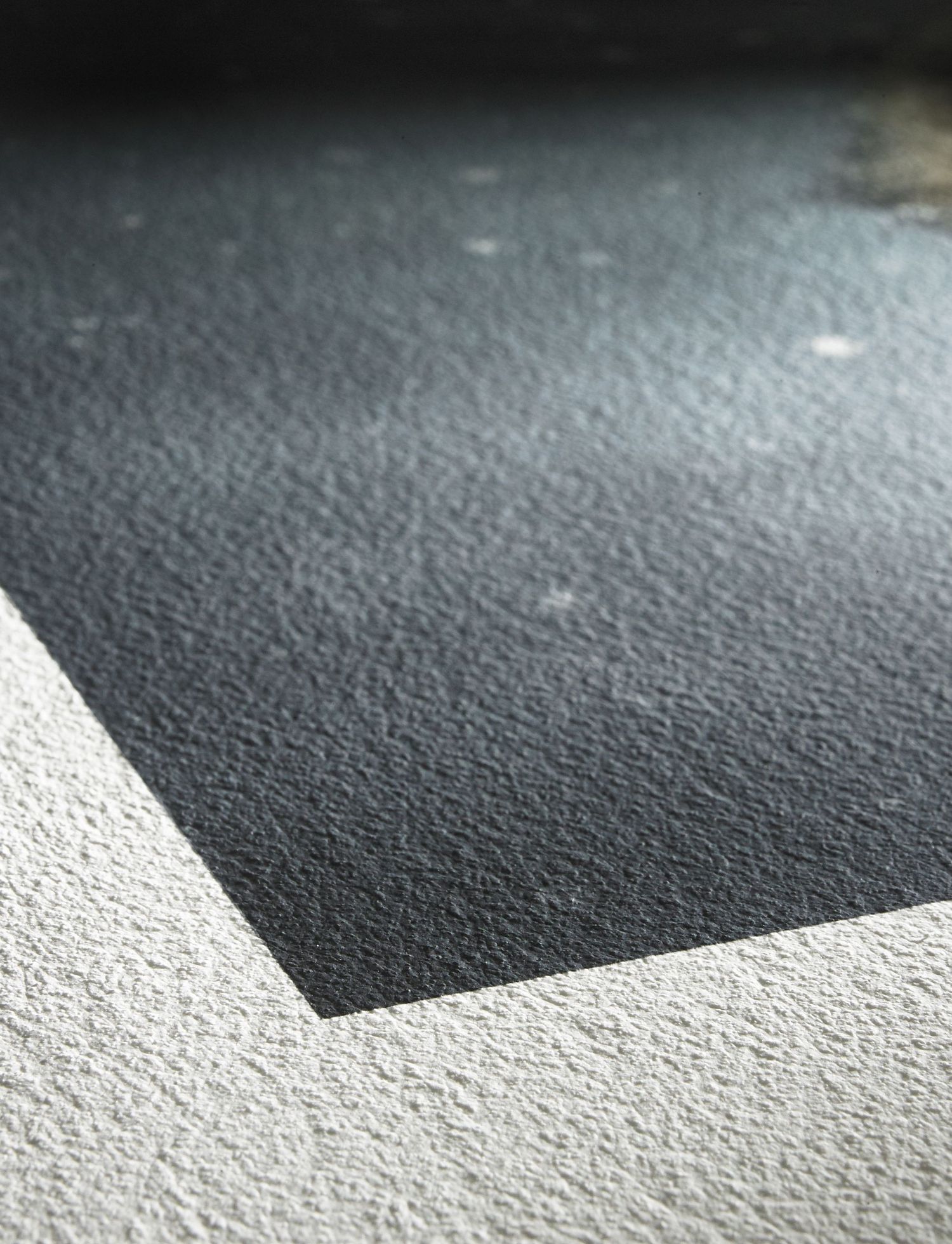 Close-up texture of dark gray asphalt surface with a white concrete border in natural sunlight.