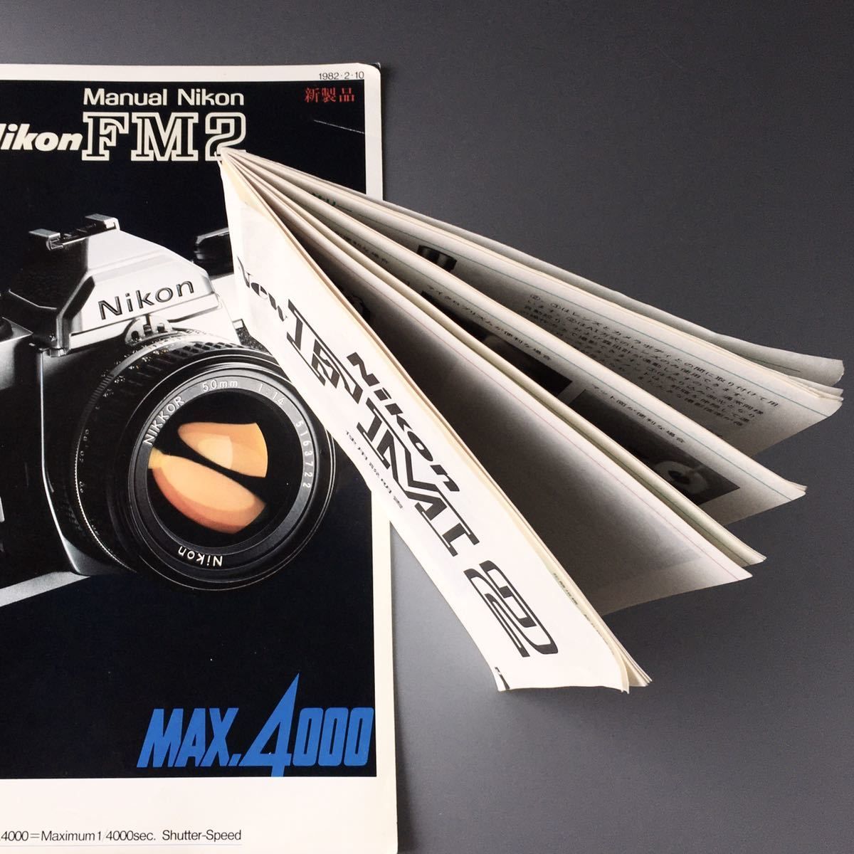 Nikon FM2 manual camera instruction booklet fanned open beside the camera catalog cover.