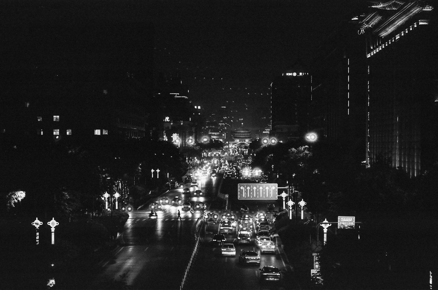 Black and white nighttime cityscape with illuminated street lights and traffic on a busy urban boulevard.