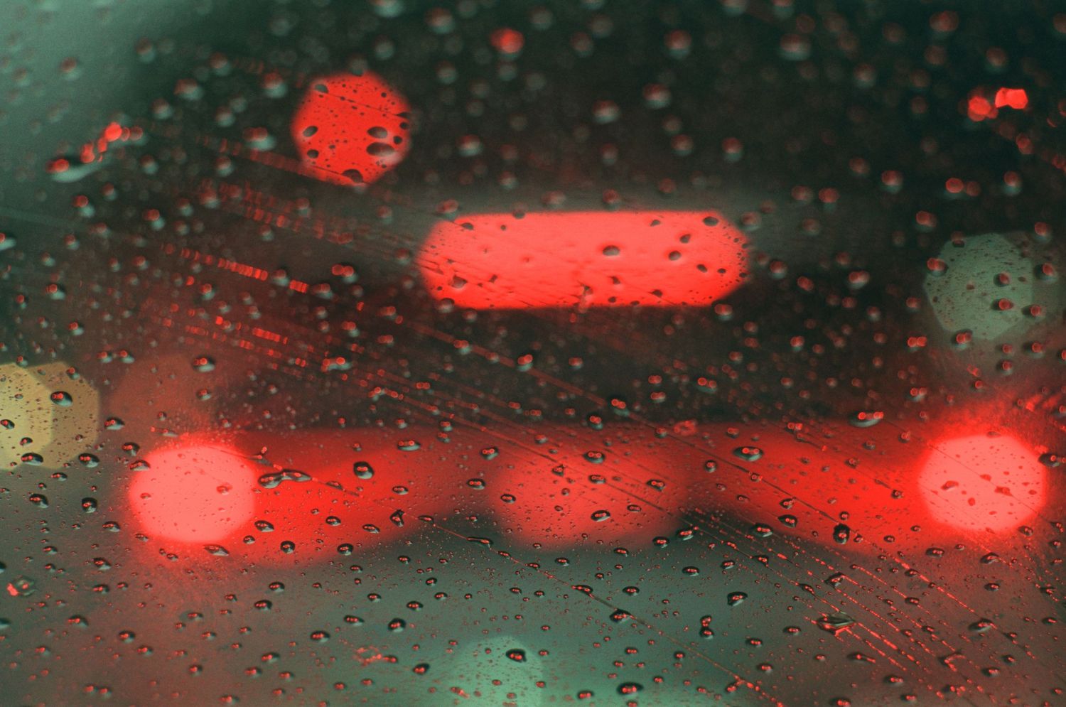 Blurred red traffic lights reflected through rain-covered car windshield on a wet night.