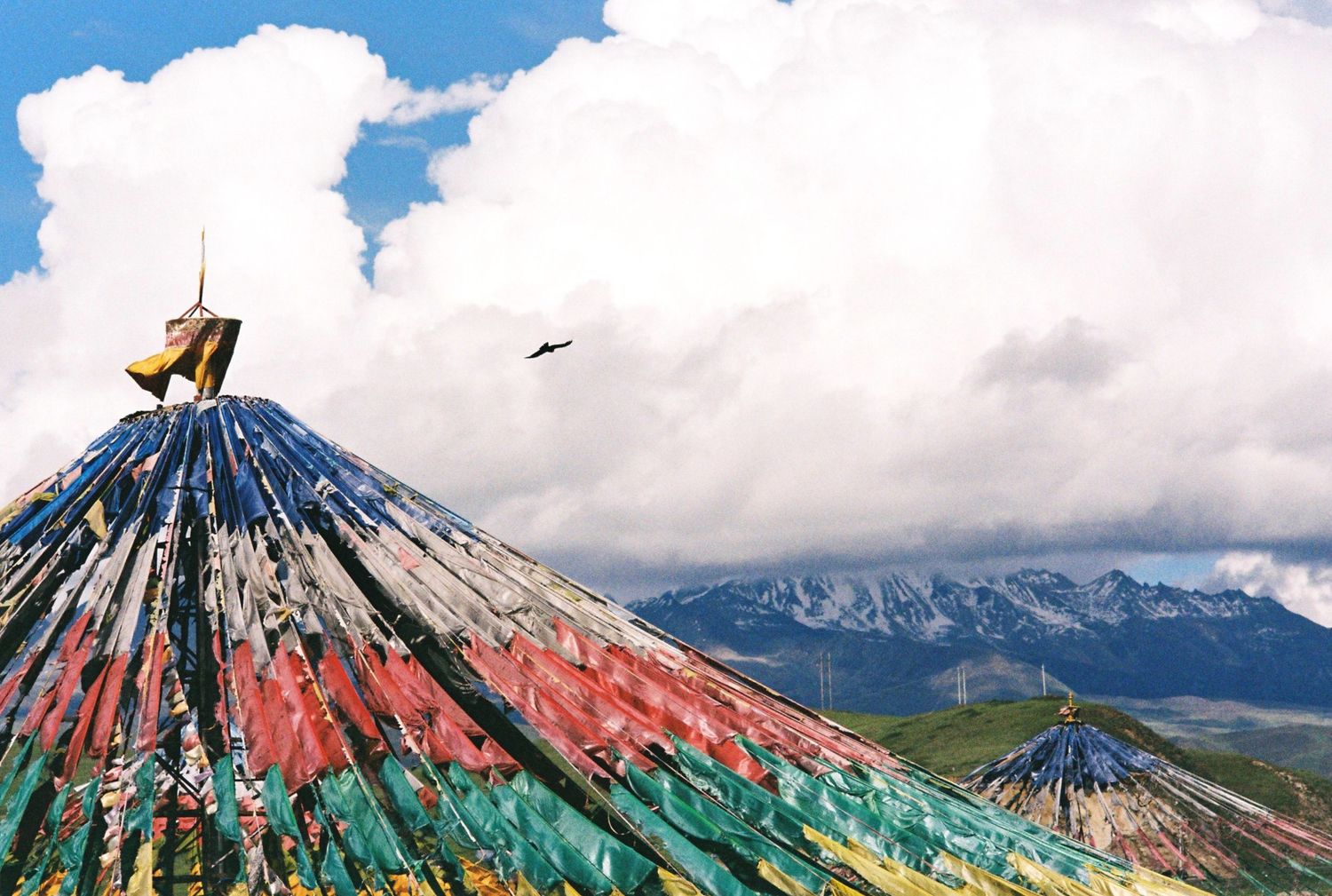 Colorful decorated tent tops with a bird in flight against dramatic clouds and mountains.