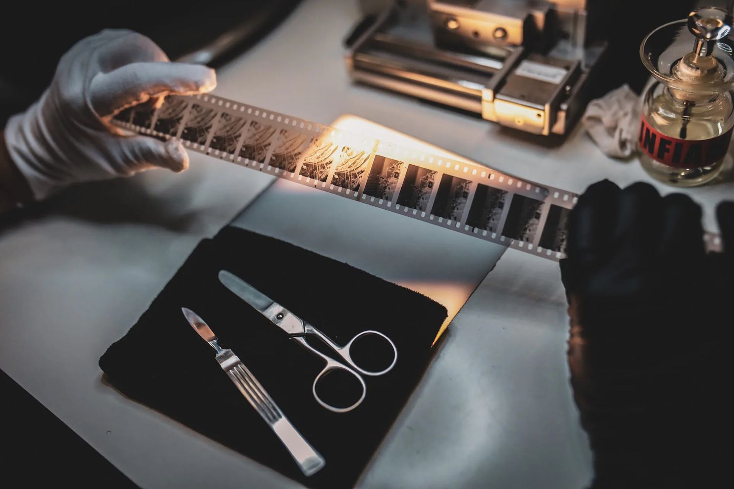 Film editor using scissors and tools to cut and splice 35mm film negatives on a light table.