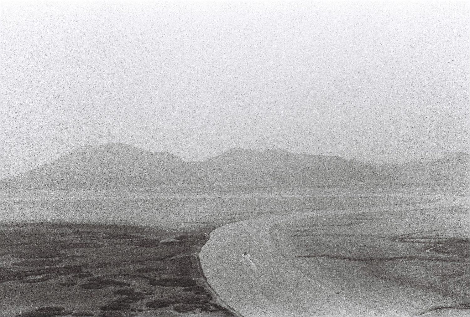 Black and white aerial photo of a winding river delta with sandy banks and misty mountains in the background.