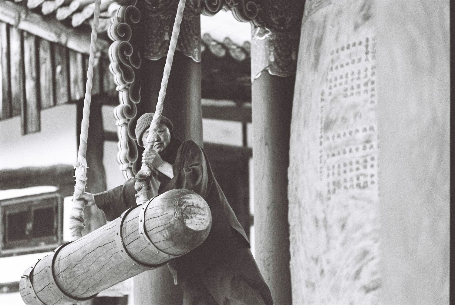 Close-up of ornate wooden beam and rope at a traditional Asian temple with stone inscription wall.