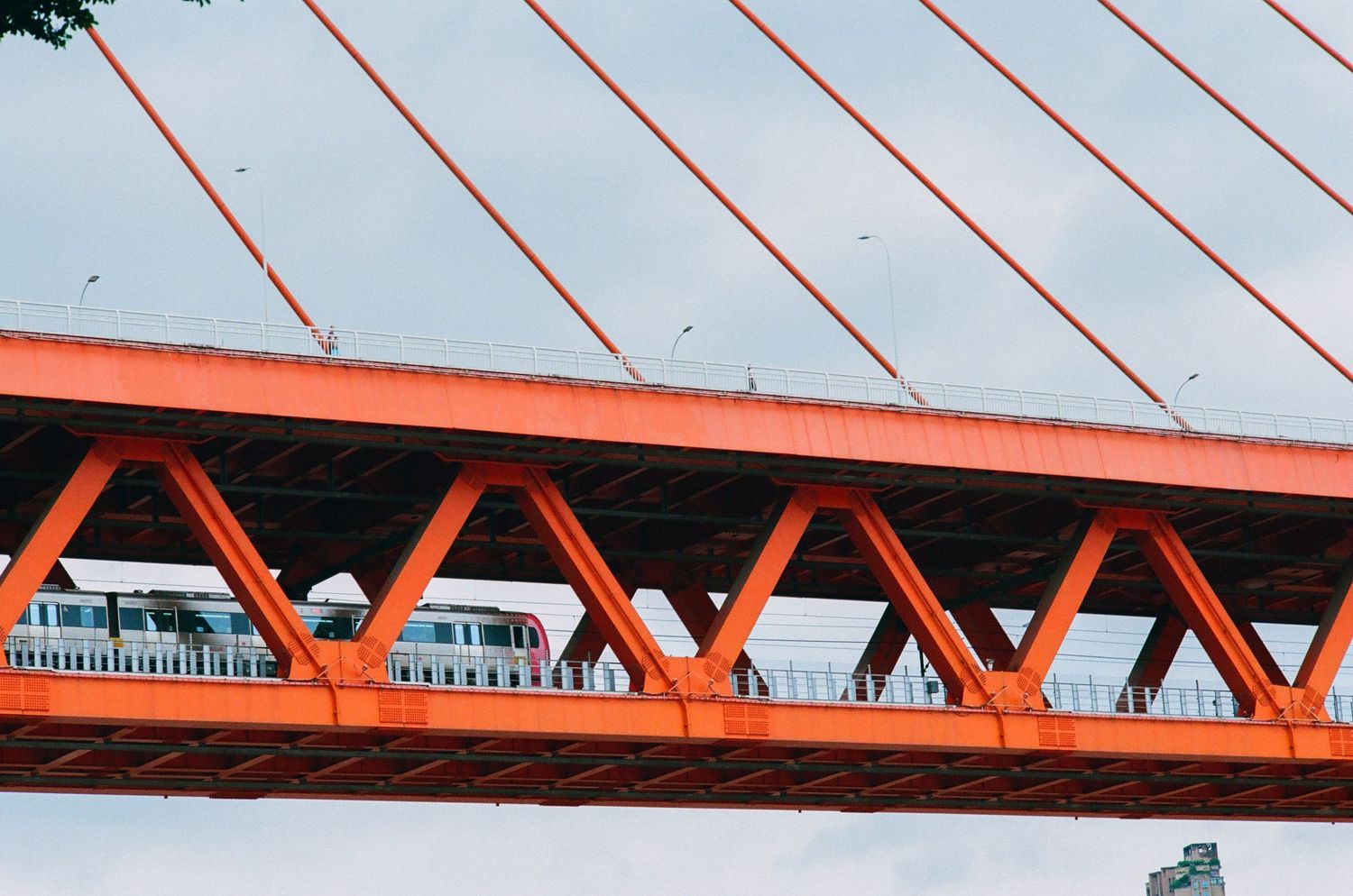 Close-up of a vibrant orange cable-stayed bridge in Chongqing with a passing train below.
