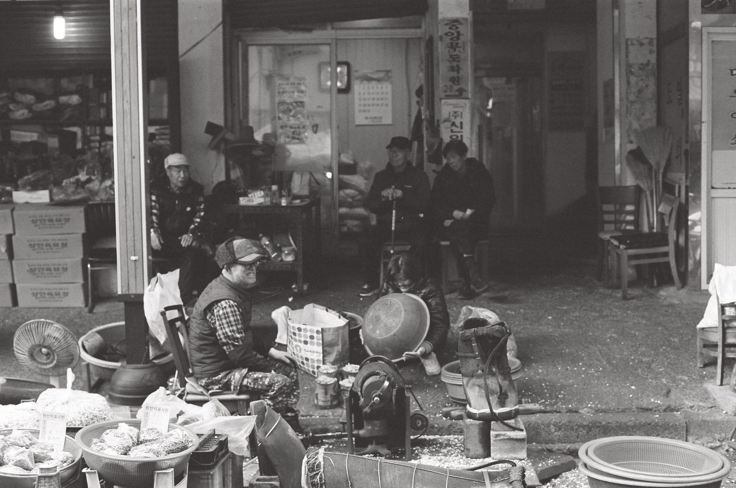 Black and white photo of a busy outdoor South Korean market stall with vendors and various goods on display.