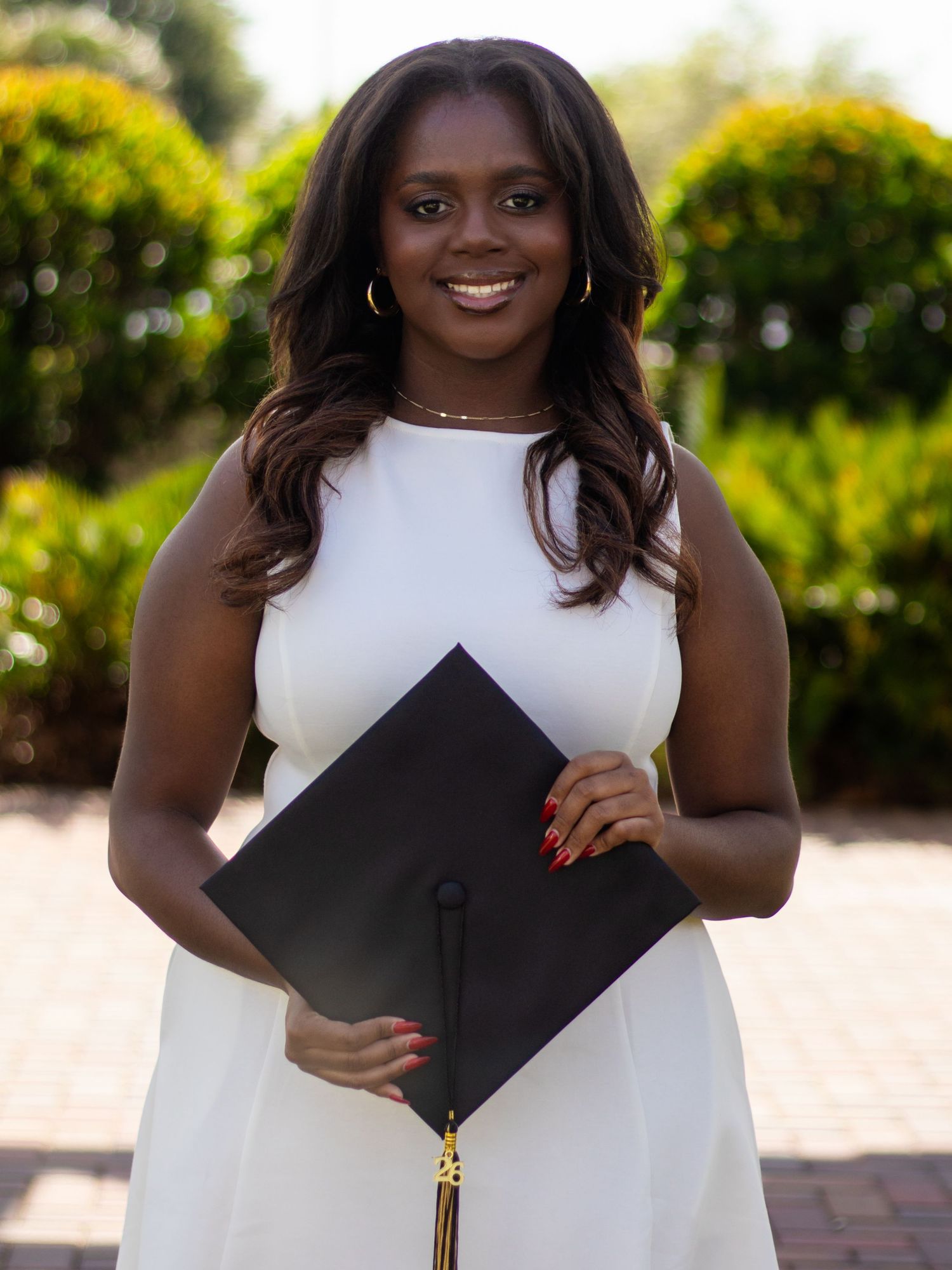High school senior girl facing the camera while holding her graduation cap at waist level