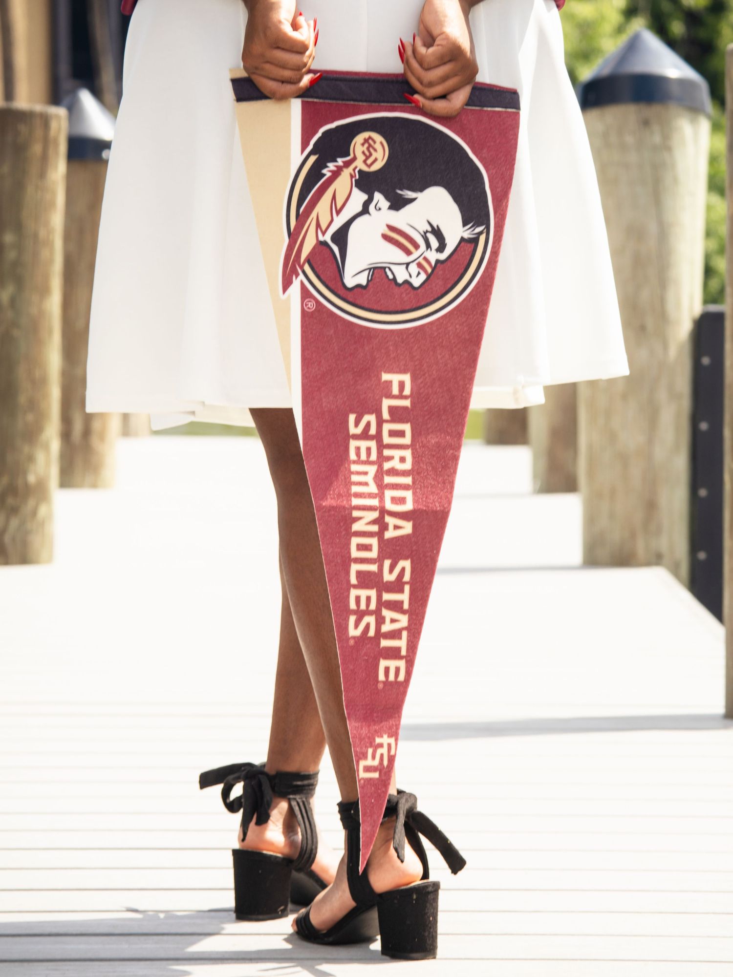 High school senior girl standing behind an FSU pennant with her legs crossed during a senior photography session