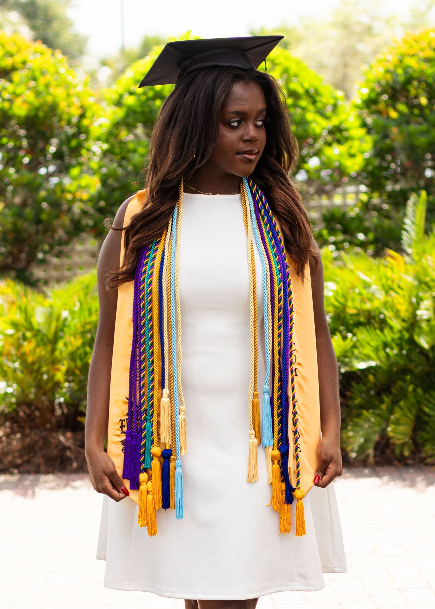 High school senior girl looking away from the camera while wearing her graduation regalia outdoors