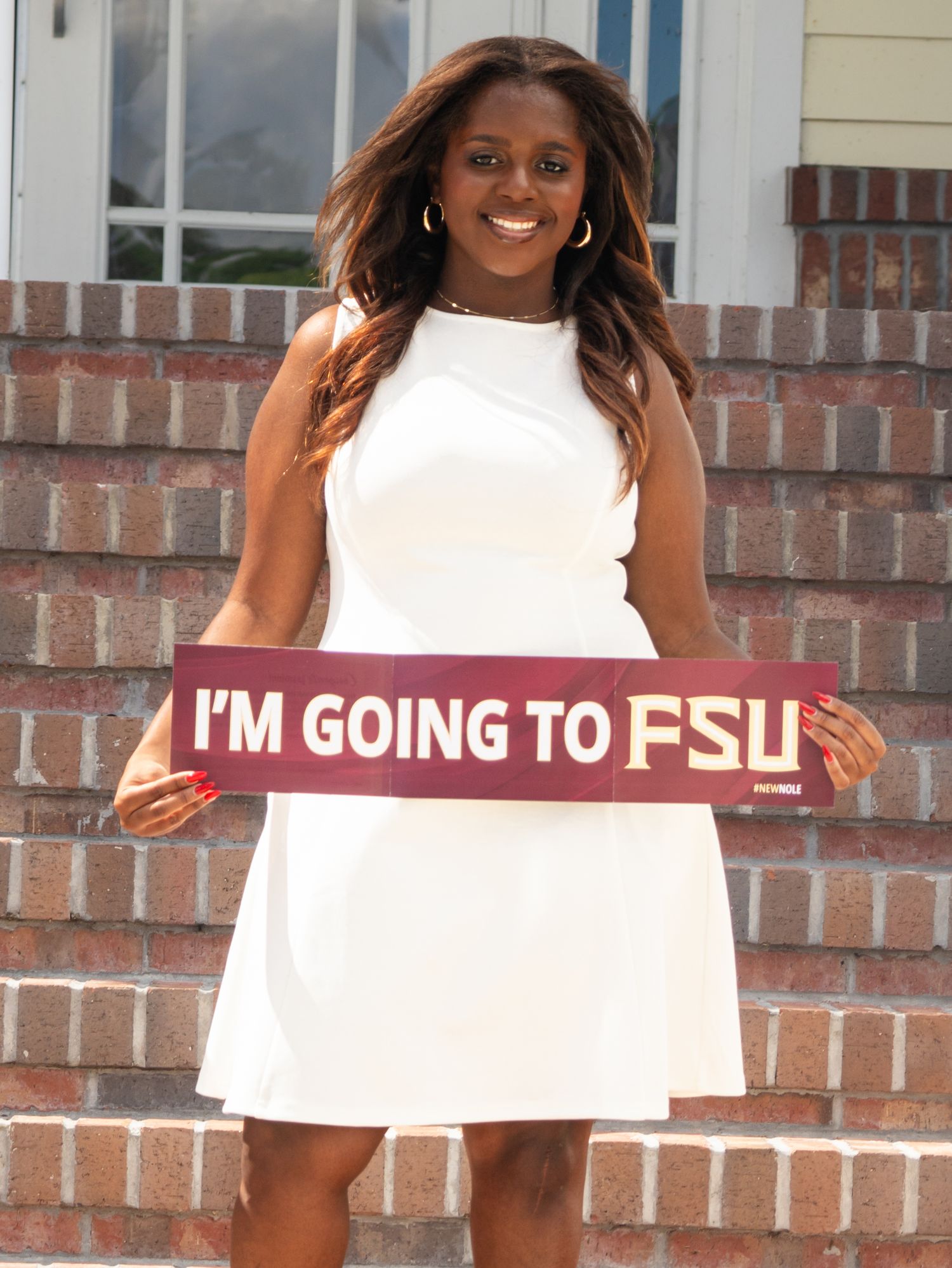 High school senior girl standing on brick stairs holding a banner announcing her plans to attend Florida State University