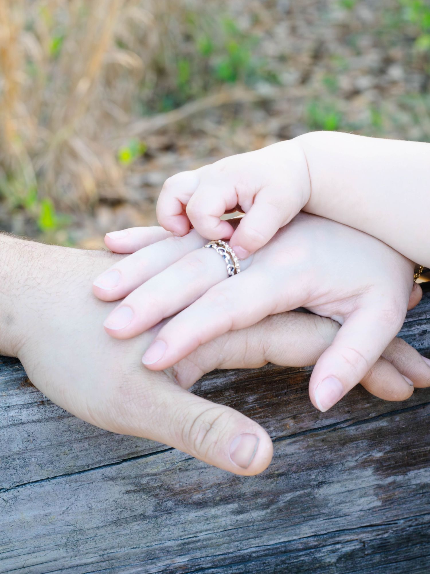 Family hands stacked together, with dad’s hand, mom’s hand, and baby’s hand during an outdoor photography session