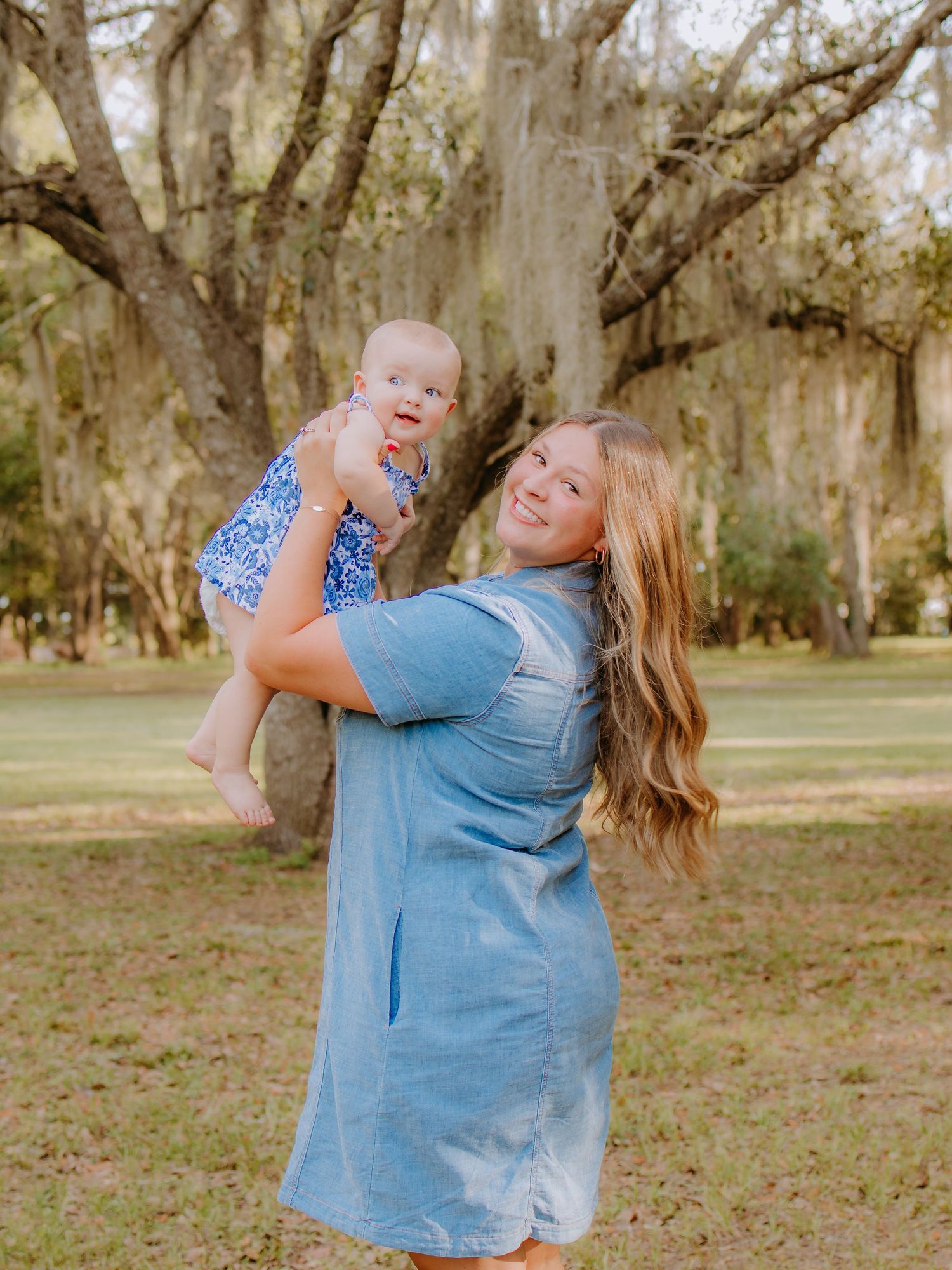 Mother smiling while holding her one-year-old daughter in the air during an outdoor mommy and me  photography session