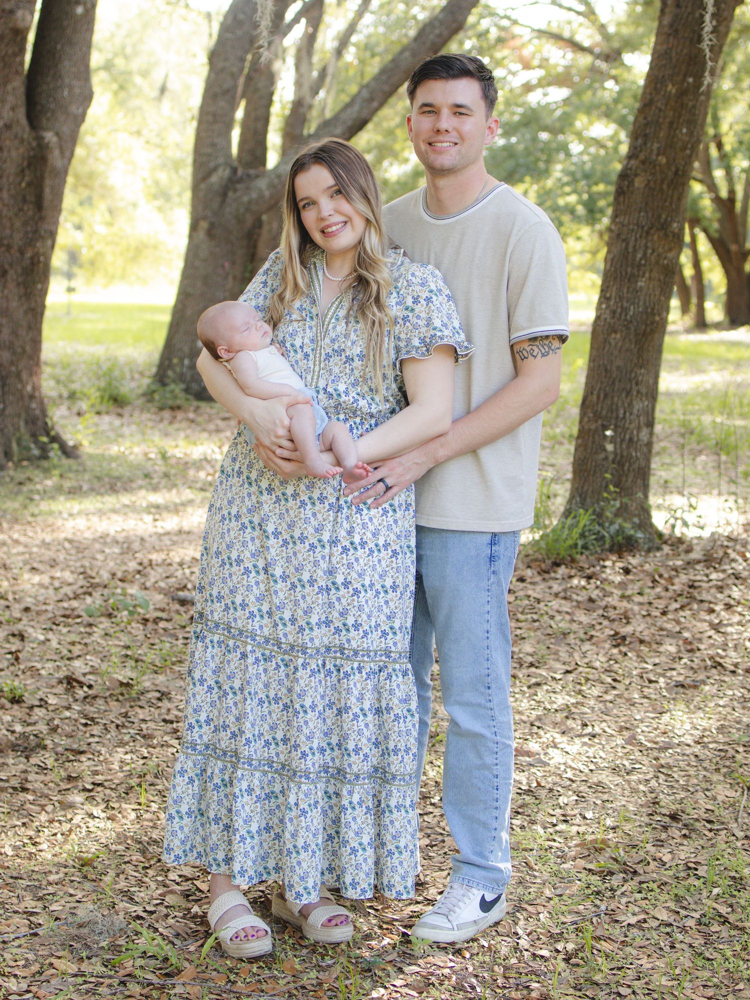 Parents standing together outdoors with the mother holding their baby during a family photography session
