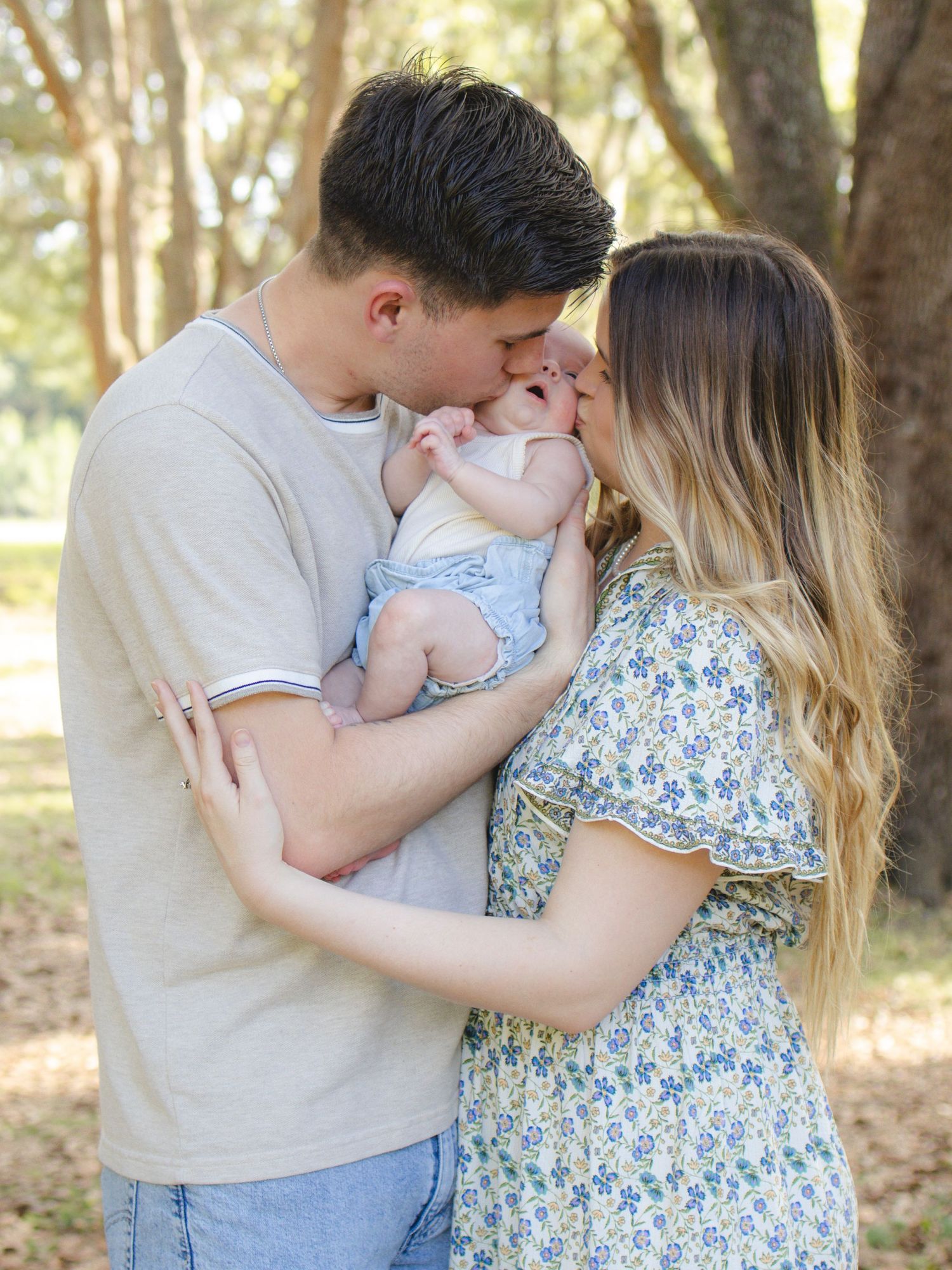 Parents kissing their baby while holding her together during an outdoor family photography session