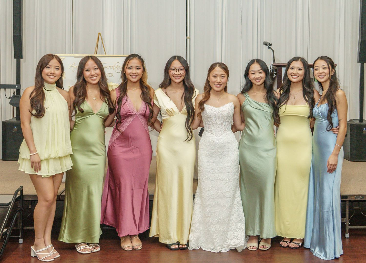 A bride in white gown poses with eight bridesmaids in colorful satin dresses at an elegant wedding reception.