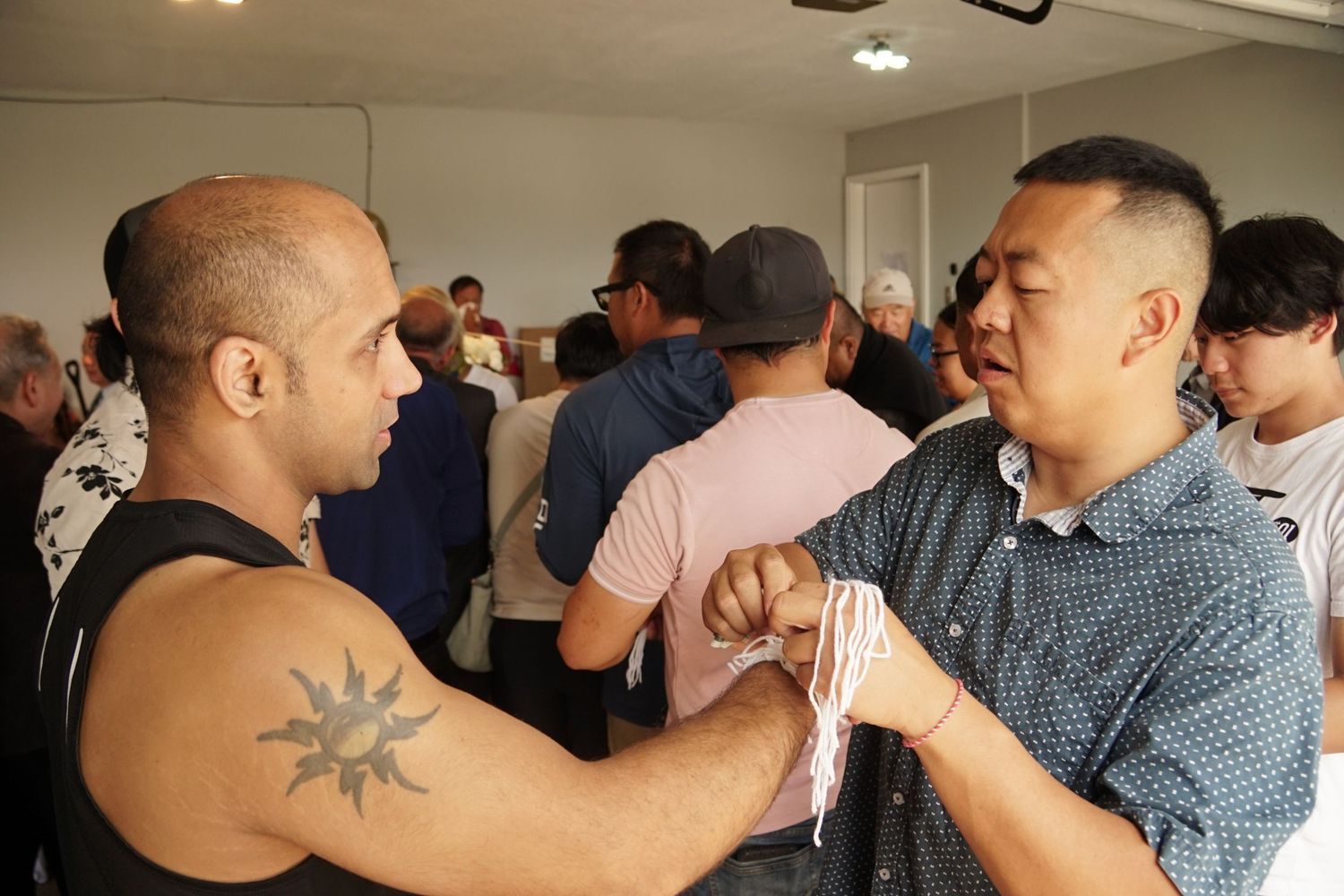 Two men interact at a casual indoor event, one with a sun tattoo on his arm.