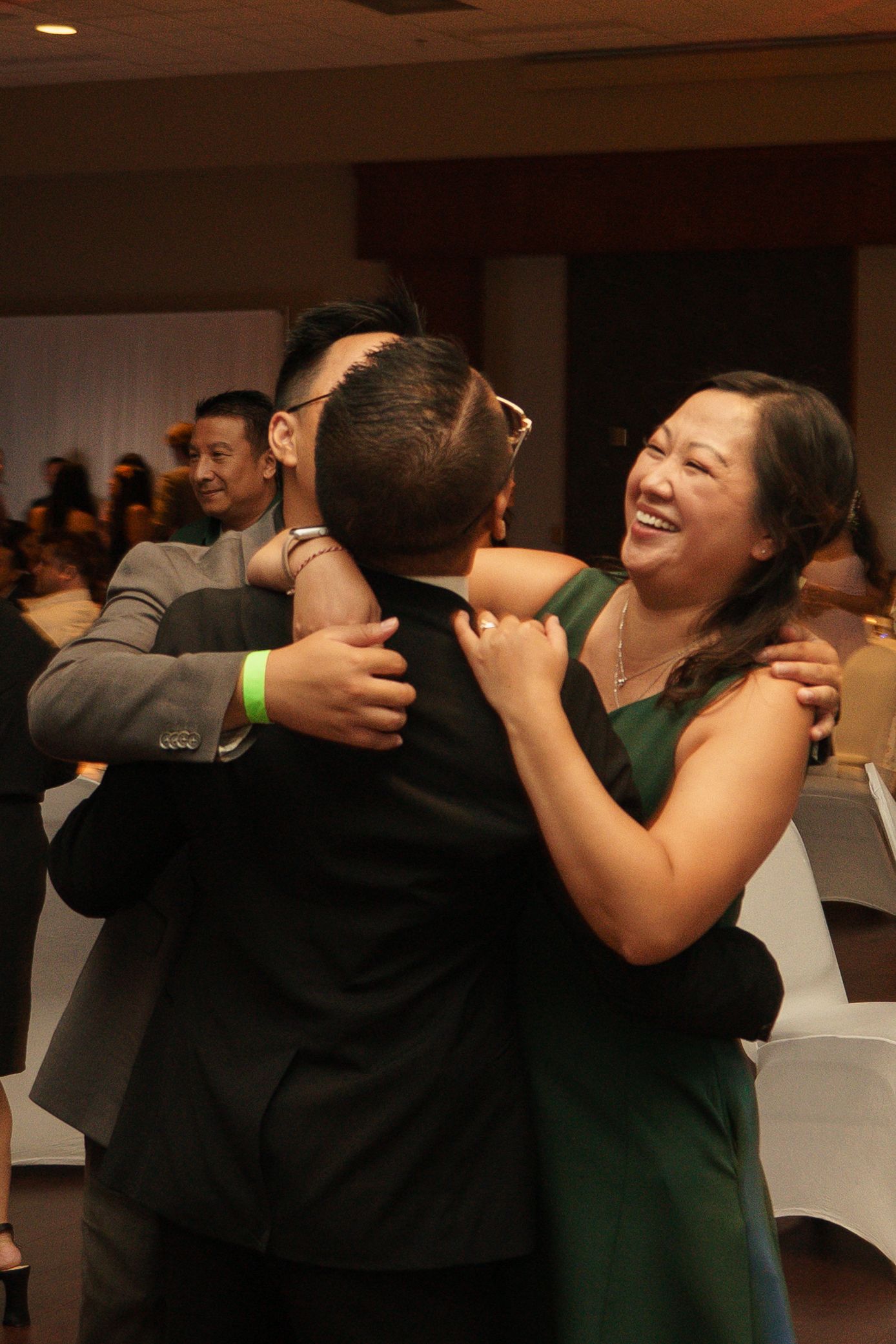 A woman in a green dress laughs joyfully while hugging a man in a black suit at a formal event.