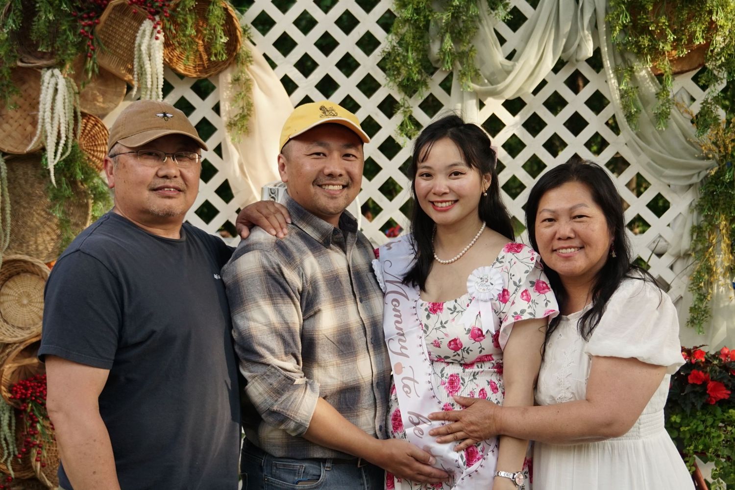 A joyful Asian family of four poses together outdoors in front of a white lattice backdrop with floral decorations.