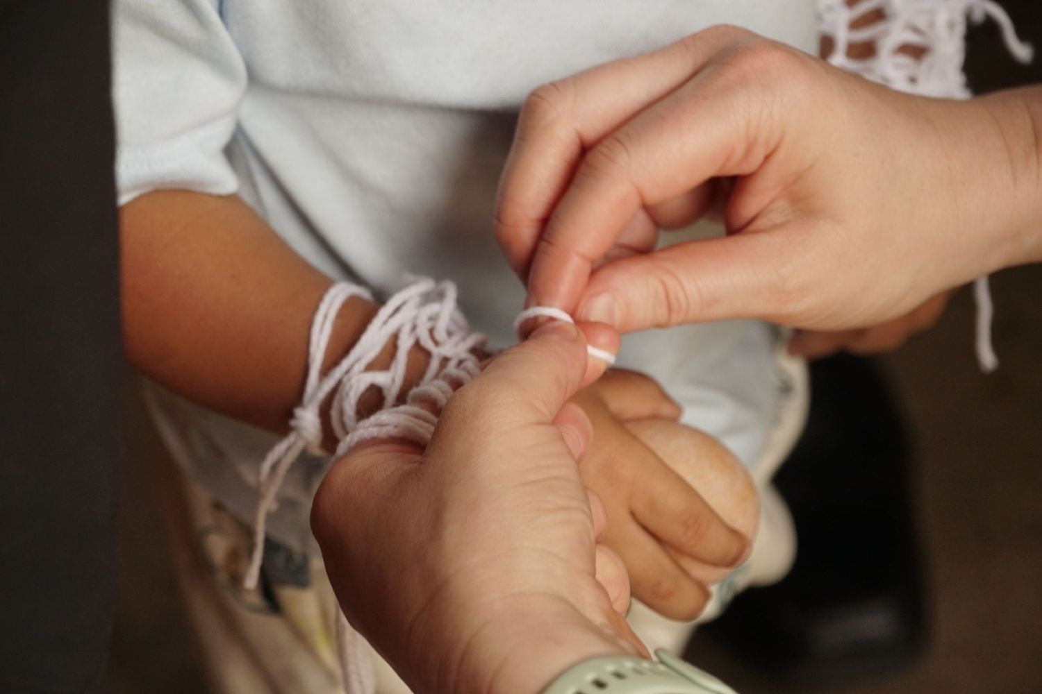 Close-up of hands tying a white string bracelet on a child's wrist.