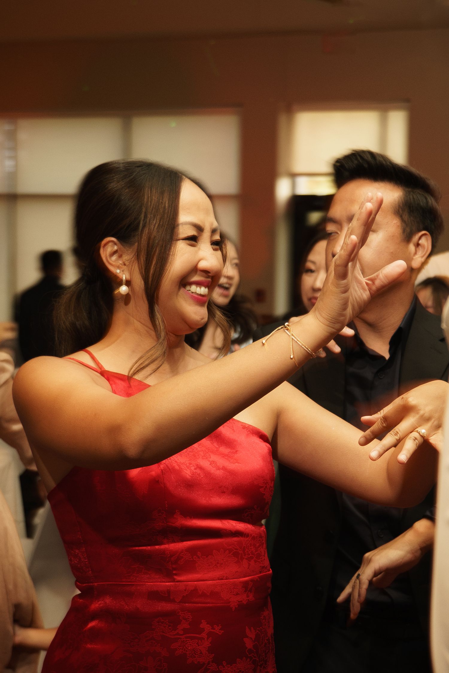 Woman in red dress smiling and dancing with guests at an Asian celebration event.