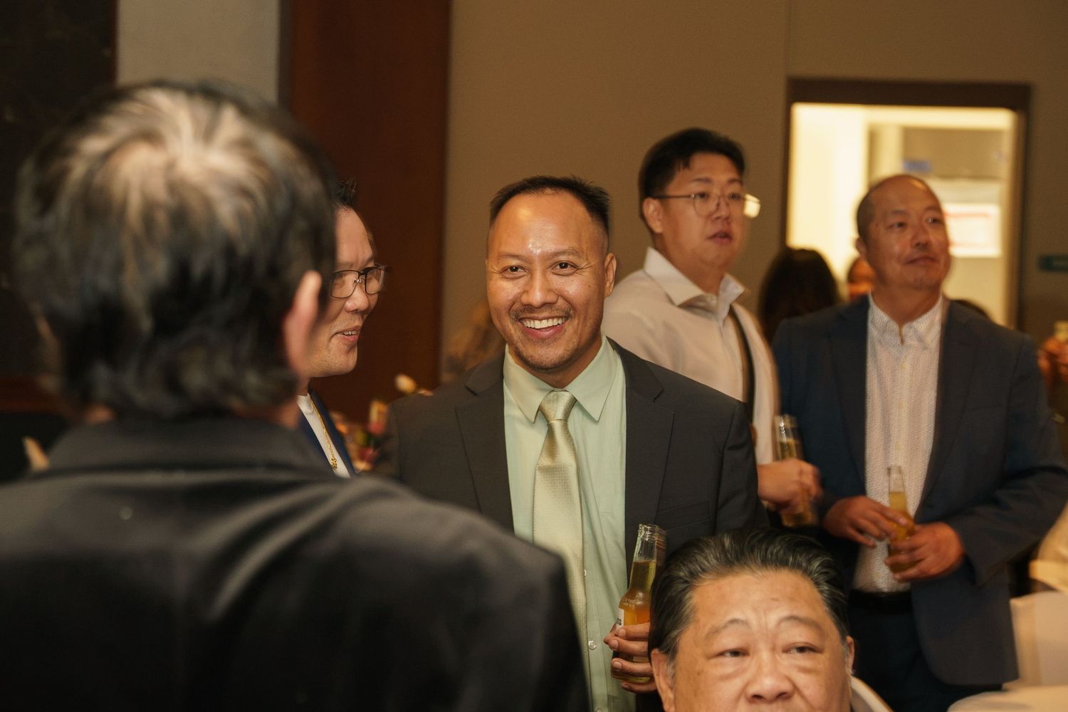 Group of Asian men socializing at a formal indoor event, smiling and conversing in elegant venue.