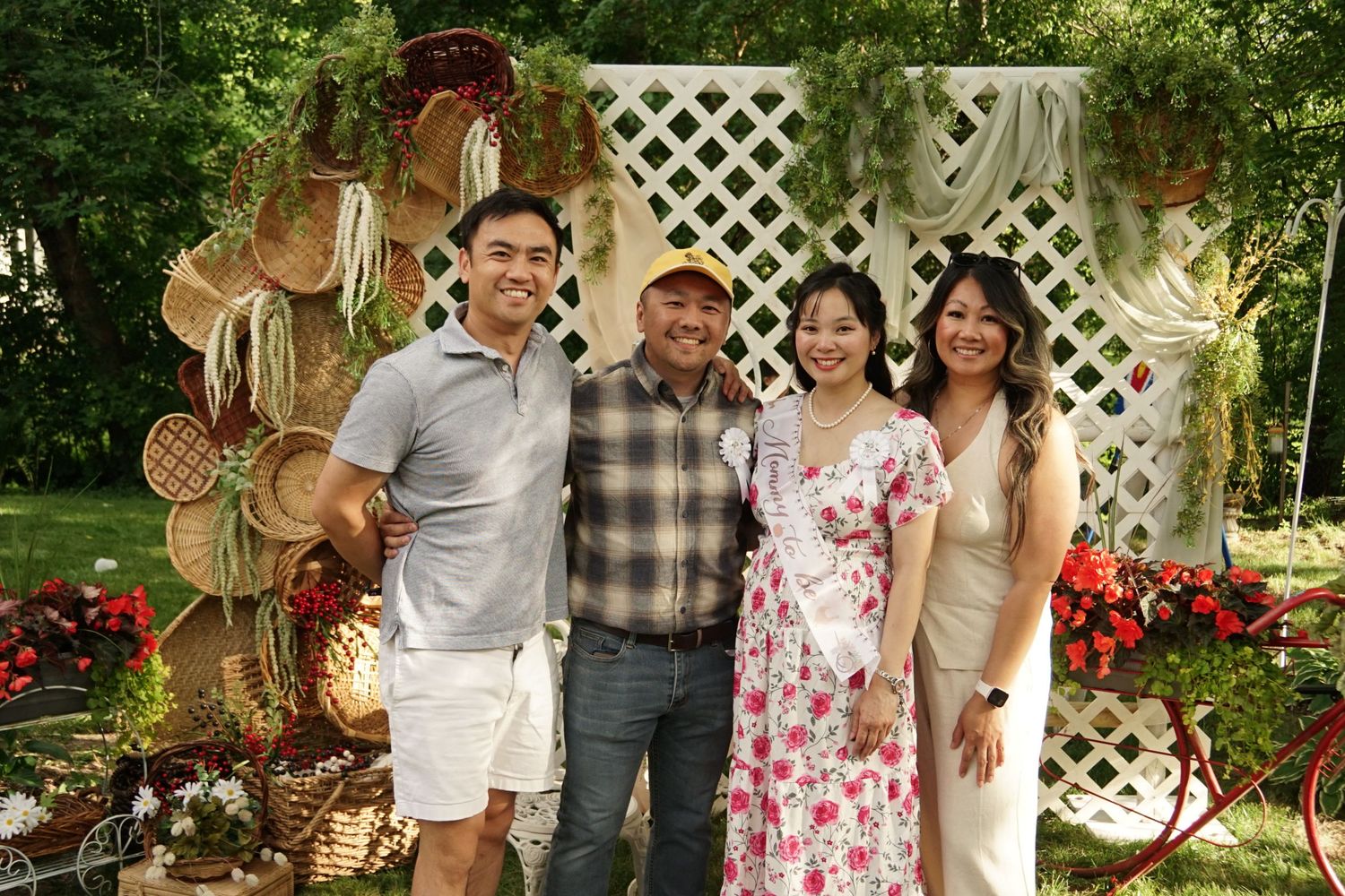 Four people smiling together outdoors at a garden party with floral decorations and wicker baskets in the background.