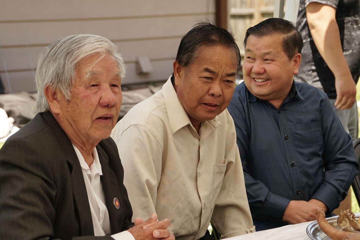 Three older men sitting together smiling at an indoor event or gathering.
