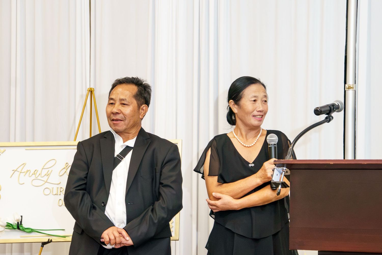 Two people in formal black attire stand together at a podium during an elegant event.